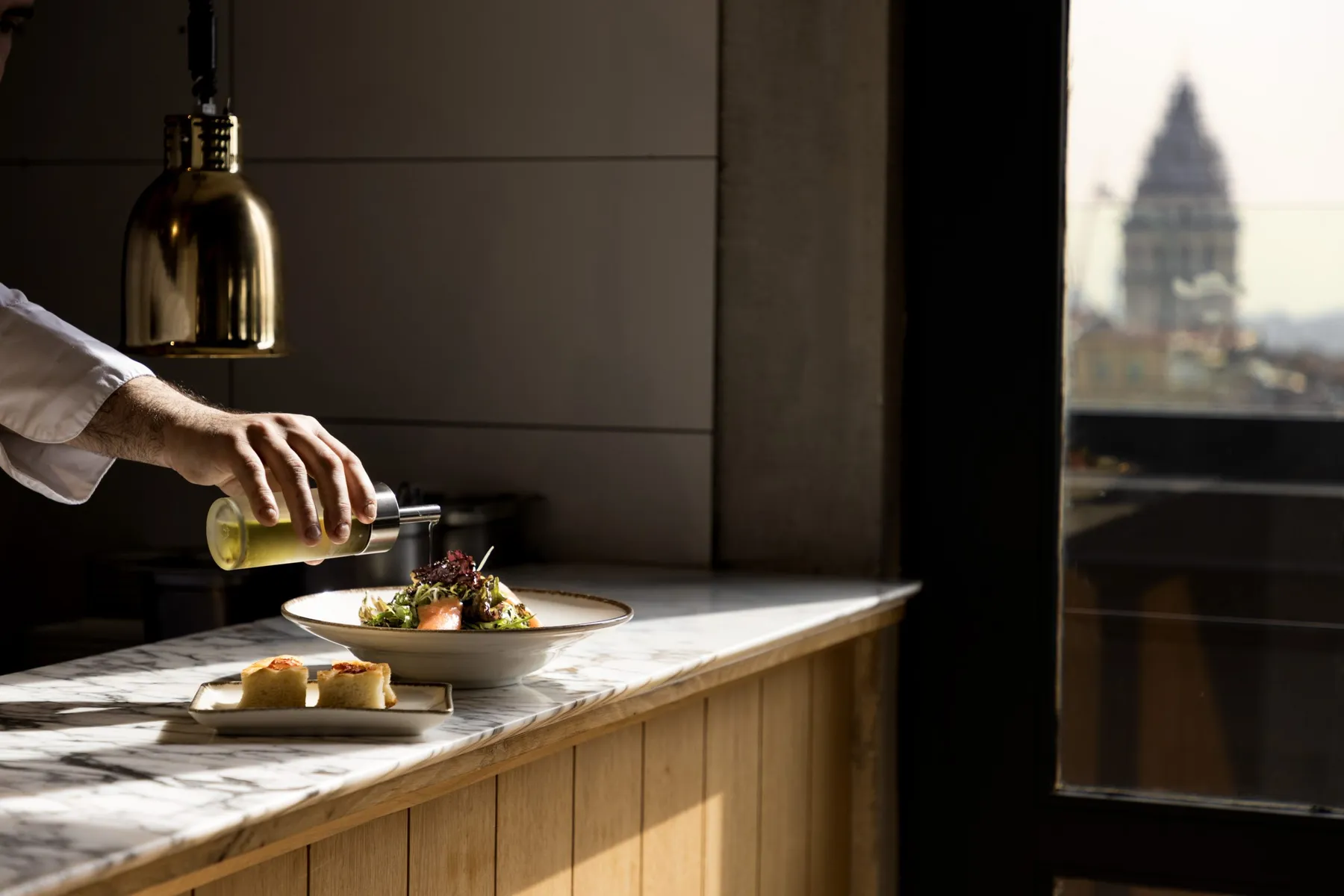 Chef finishing a dish, Galata Tower through the window